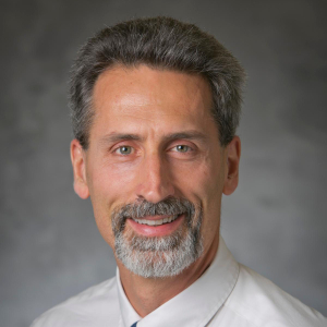 a man with dark gray hair and a goatee wearing a light blue shirt and white button up shirt