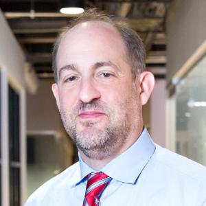 a man with gray hair and a light beard wearing a light blue shirt and red tie
